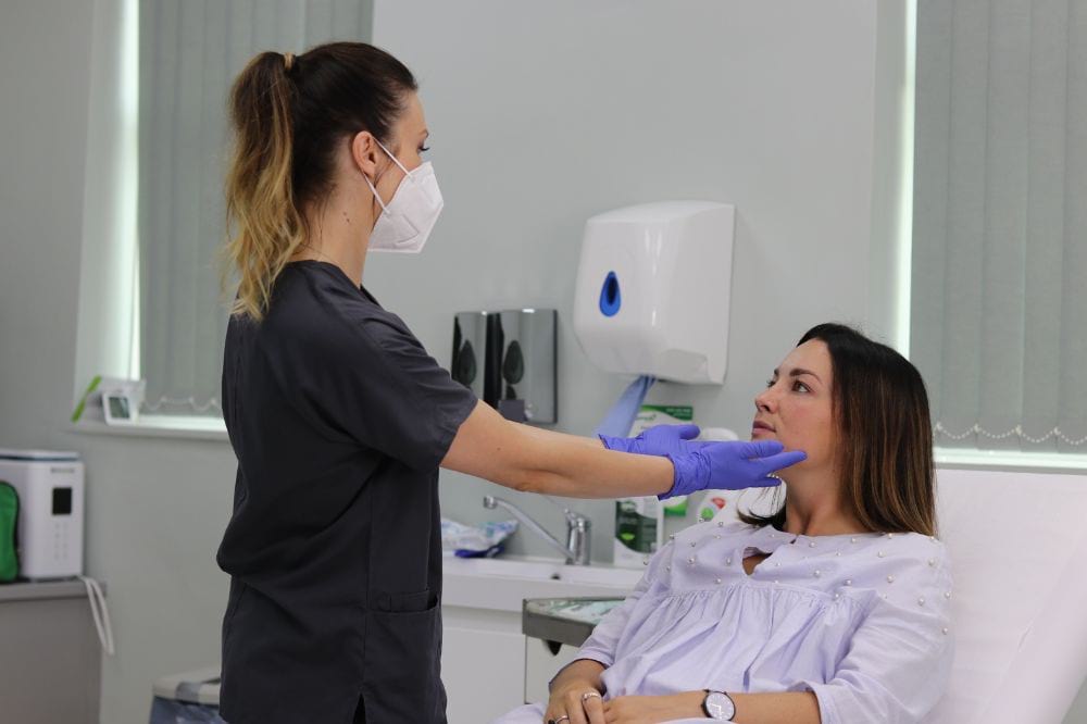 Aesthetic practitioner wearing facemask does facial analysis on a patient