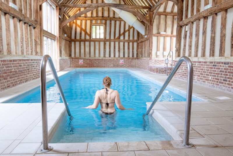 woman walking into swimming pool with historic beams in ceiling 