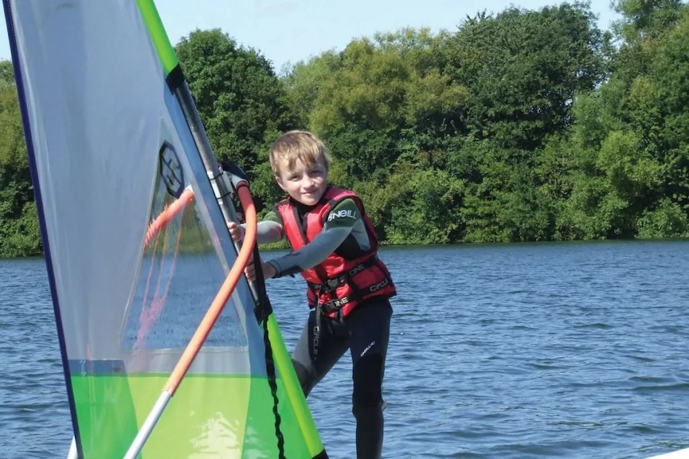 A boy windsurfing with Aqua Sport Company at Mercers Country Park near Redhill, Surrey.
